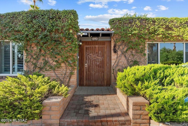 doorway to property featuring a tile roof and brick siding