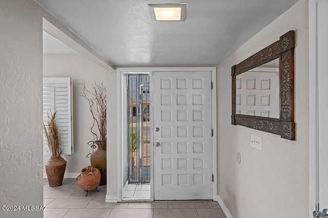 tiled entryway featuring baseboards, a textured ceiling, and a textured wall