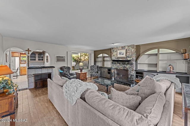 living room with built in features, arched walkways, wood finished floors, and a stone fireplace