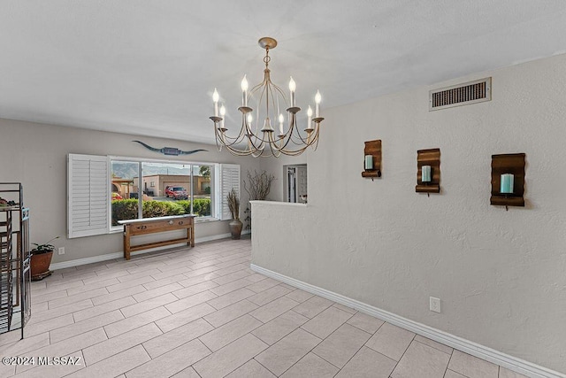 interior space with a chandelier, a textured wall, visible vents, and baseboards