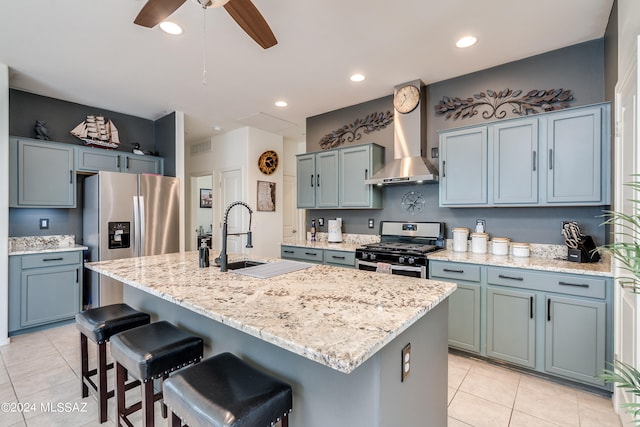 kitchen with ceiling fan, an island with sink, wall chimney exhaust hood, appliances with stainless steel finishes, and light tile patterned floors