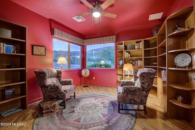 sitting room with a mountain view, hardwood / wood-style floors, and ceiling fan