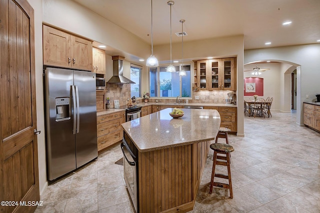 kitchen featuring decorative backsplash, a center island, wall chimney exhaust hood, and appliances with stainless steel finishes