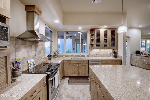 kitchen featuring pendant lighting, sink, range hood, stainless steel appliances, and light stone counters