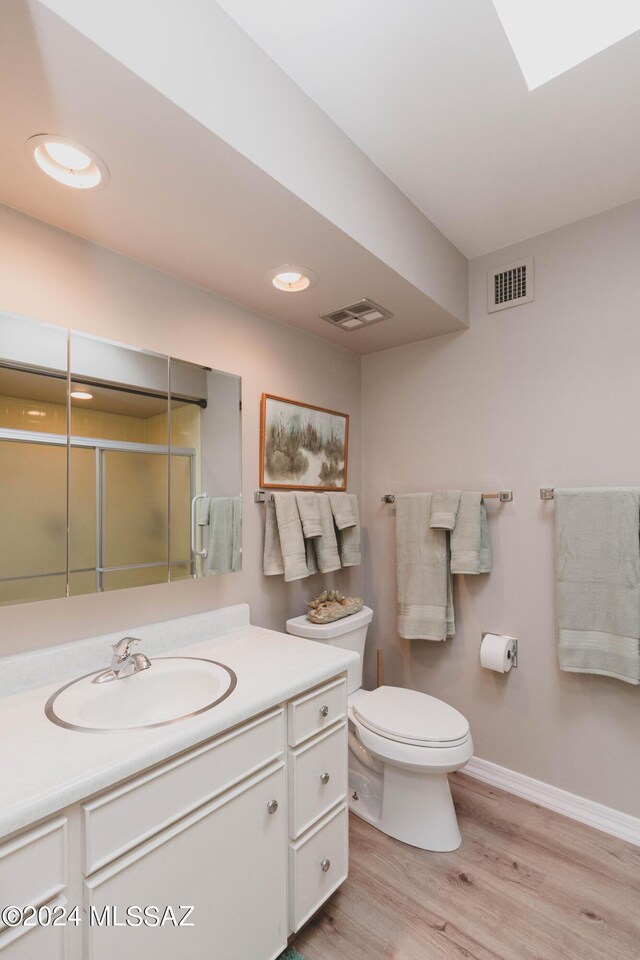 bathroom with toilet, an enclosed shower, wood-type flooring, a skylight, and vanity