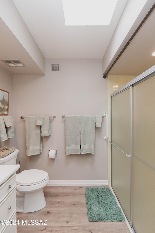 bathroom featuring toilet, wood-type flooring, a shower with shower door, a skylight, and vanity