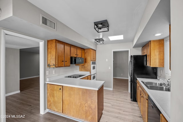 kitchen with light wood-type flooring, kitchen peninsula, sink, and black appliances