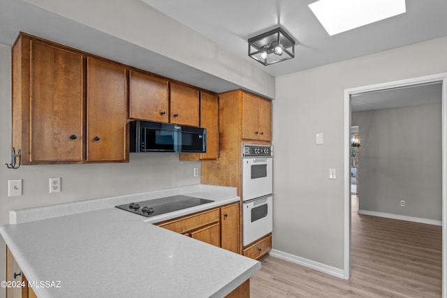 kitchen featuring a skylight, light hardwood / wood-style floors, and black appliances