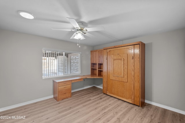 unfurnished office featuring light hardwood / wood-style floors, built in desk, and ceiling fan