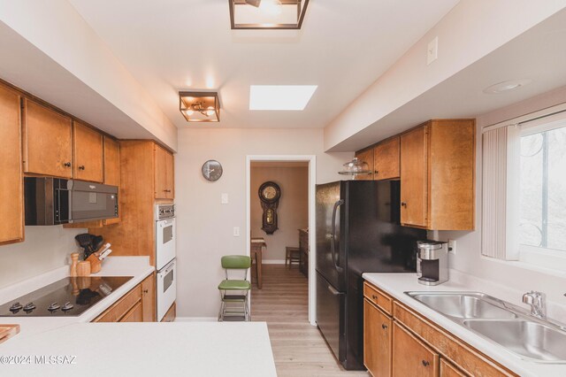 kitchen with a skylight, black appliances, sink, kitchen peninsula, and light wood-type flooring