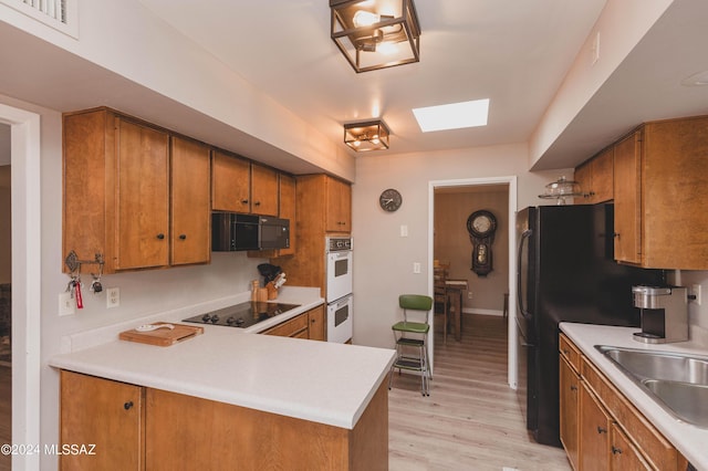 kitchen featuring light wood-type flooring, kitchen peninsula, sink, and black appliances