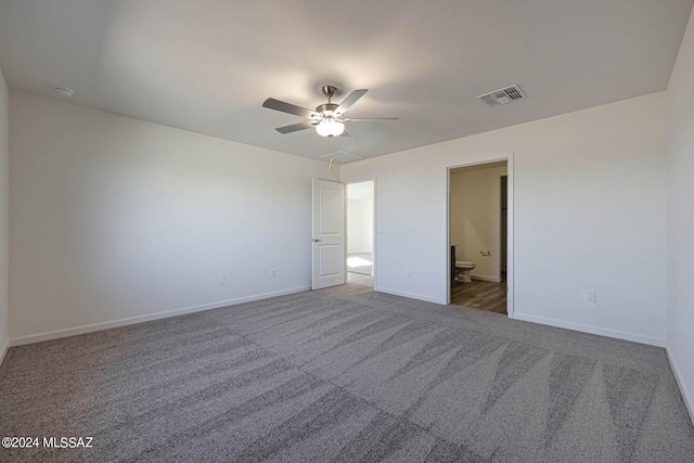 unfurnished bedroom featuring ceiling fan, ensuite bathroom, and dark carpet