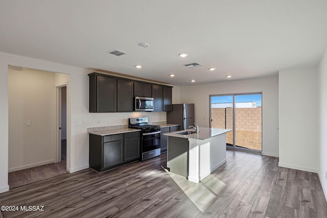 kitchen featuring hardwood / wood-style floors, appliances with stainless steel finishes, sink, light stone counters, and a center island with sink