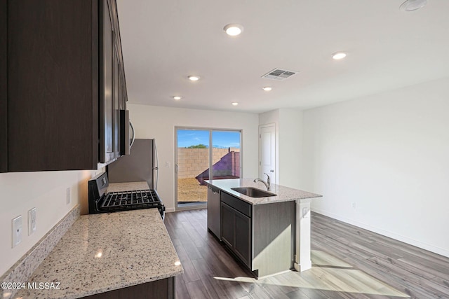 kitchen featuring appliances with stainless steel finishes, sink, hardwood / wood-style flooring, a kitchen island with sink, and light stone counters