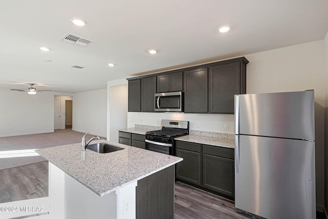 kitchen featuring ceiling fan, a center island with sink, sink, light stone countertops, and stainless steel appliances