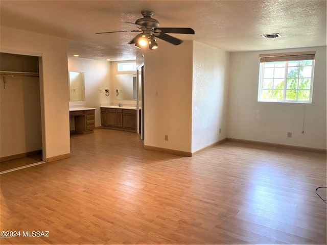 unfurnished bedroom featuring a closet, connected bathroom, a textured ceiling, and light hardwood / wood-style flooring