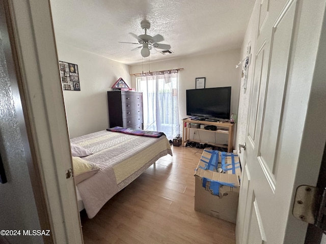 bedroom featuring ceiling fan, light hardwood / wood-style floors, and a textured ceiling