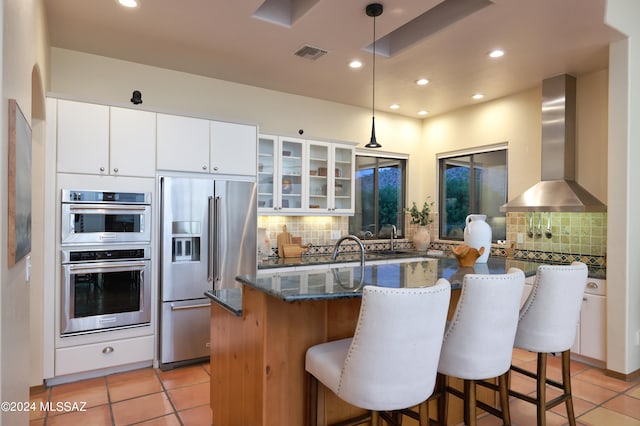 kitchen with white cabinets, tasteful backsplash, stainless steel appliances, wall chimney exhaust hood, and decorative light fixtures