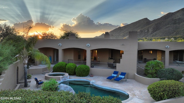 back house at dusk featuring a swimming pool with hot tub and a patio