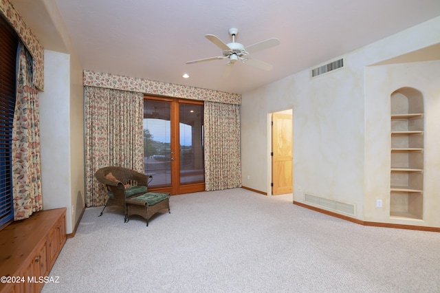 sitting room featuring light carpet, built in shelves, and ceiling fan