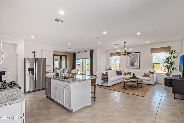 kitchen featuring sink, white cabinetry, light stone counters, stainless steel appliances, and a kitchen island with sink