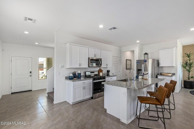 kitchen featuring a breakfast bar, a kitchen island with sink, white cabinetry, stainless steel appliances, and light stone counters