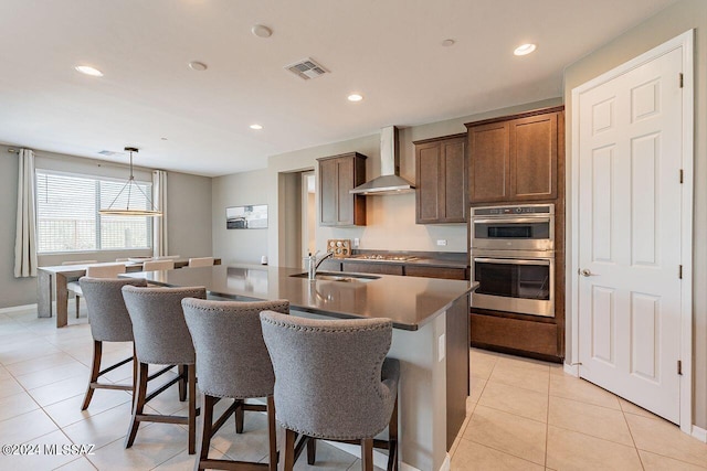 kitchen with visible vents, an island with sink, decorative light fixtures, stainless steel appliances, and wall chimney range hood