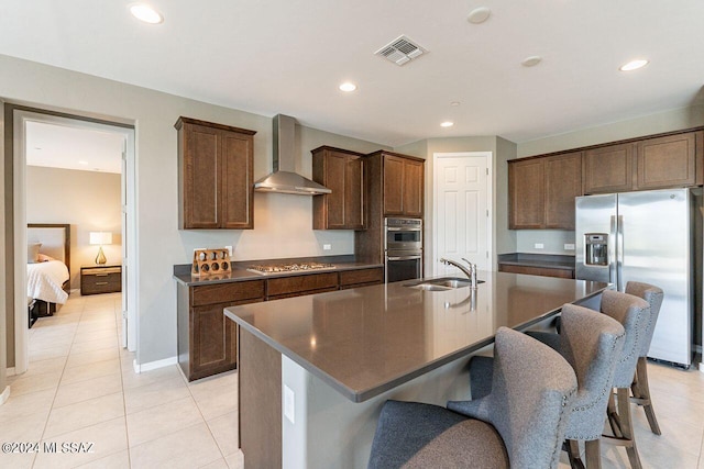 kitchen featuring a kitchen island with sink, stainless steel appliances, a sink, visible vents, and wall chimney range hood