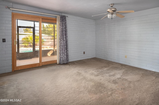 spare room featuring carpet floors, ceiling fan, and brick wall