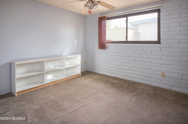 carpeted empty room featuring ceiling fan, brick wall, and a textured ceiling