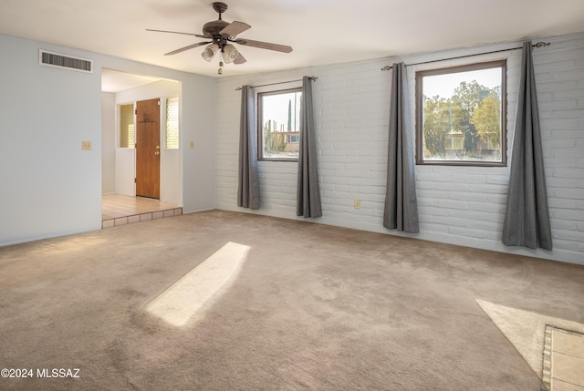 carpeted spare room featuring ceiling fan and brick wall