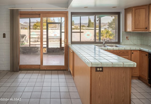 kitchen featuring sink, decorative backsplash, tile counters, light tile patterned flooring, and kitchen peninsula