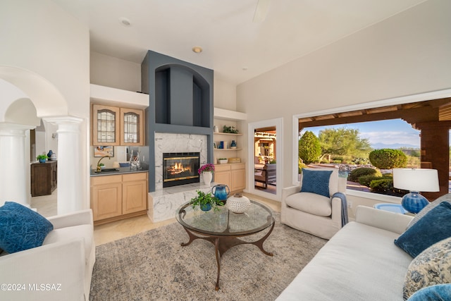 living room with a premium fireplace, decorative columns, high vaulted ceiling, and built in features