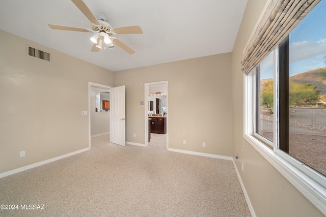 unfurnished bedroom with ceiling fan, ensuite bath, and light colored carpet