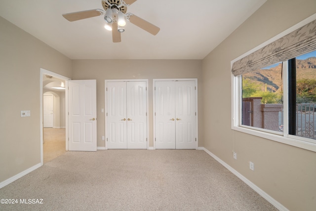 unfurnished bedroom with carpet floors, two closets, and ceiling fan