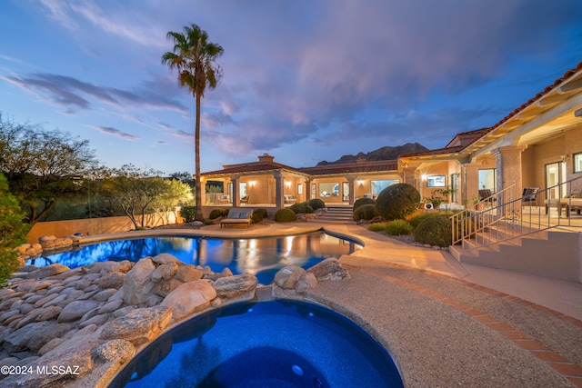 pool at dusk with an in ground hot tub and a patio area