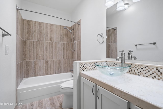 full bathroom featuring toilet, tiled shower / bath, vanity, hardwood / wood-style flooring, and backsplash