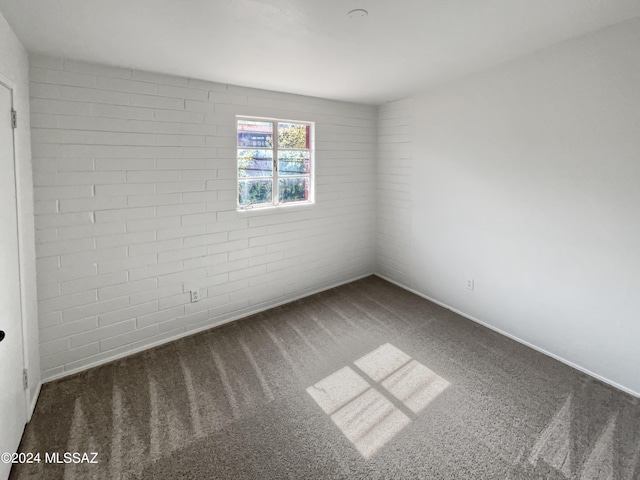 carpeted spare room with brick wall