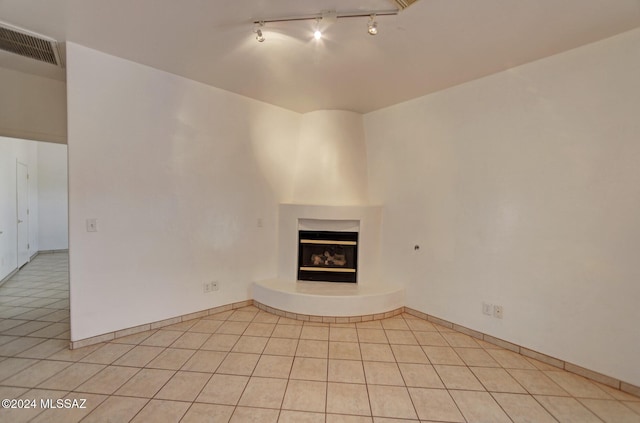 unfurnished living room featuring a fireplace, light tile patterned floors, and rail lighting