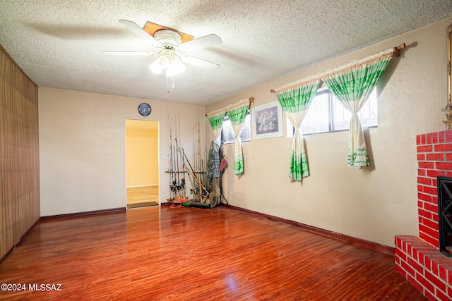 spare room featuring ceiling fan, a fireplace, wood-type flooring, and a textured ceiling