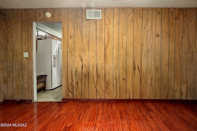 unfurnished room featuring light hardwood / wood-style flooring, a textured ceiling, and wooden walls