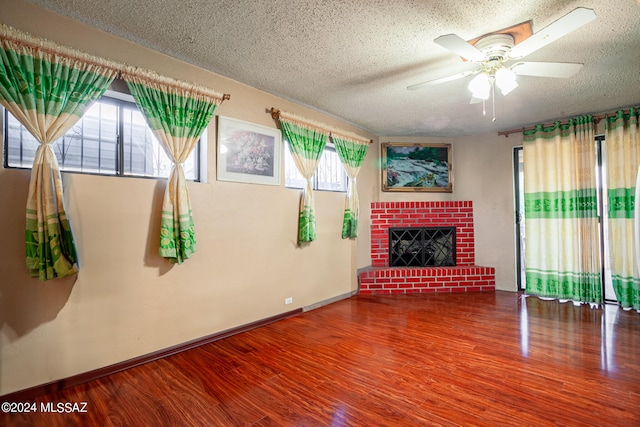 living room featuring ceiling fan, a fireplace, a textured ceiling, and hardwood / wood-style flooring