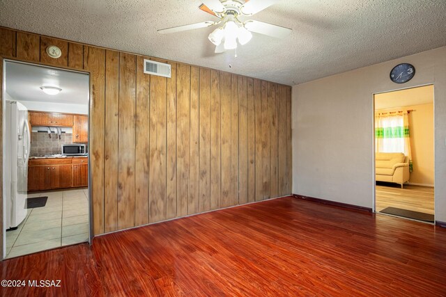 empty room featuring wood walls, a textured ceiling, ceiling fan, and hardwood / wood-style floors