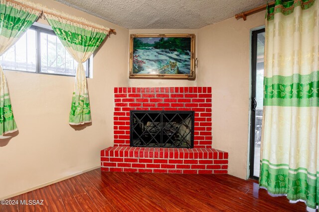 unfurnished living room featuring wood-type flooring, a textured ceiling, and a brick fireplace