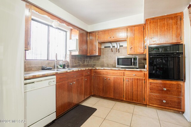 kitchen with tasteful backsplash, white dishwasher, sink, light tile patterned flooring, and black oven