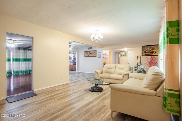 living room featuring ceiling fan with notable chandelier and light wood-type flooring