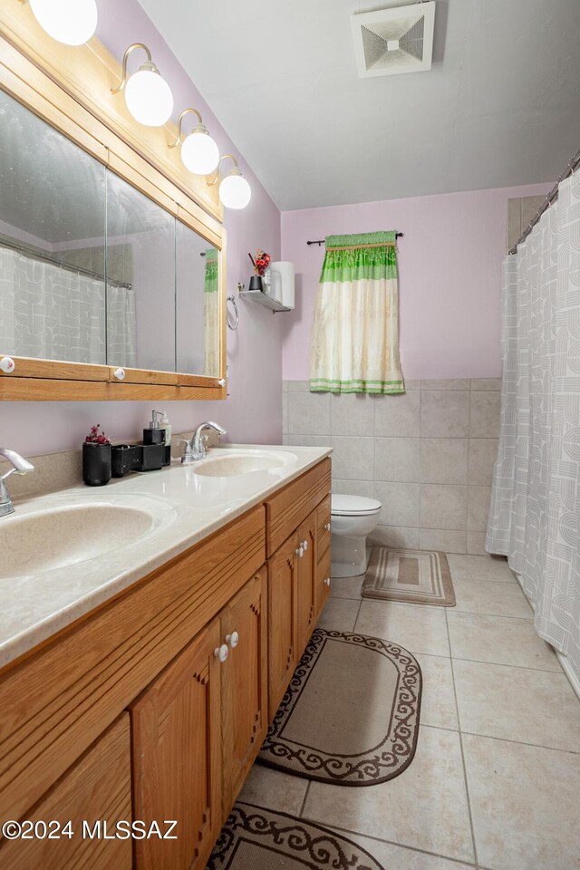 bathroom featuring tile patterned flooring, tile walls, toilet, and double sink vanity