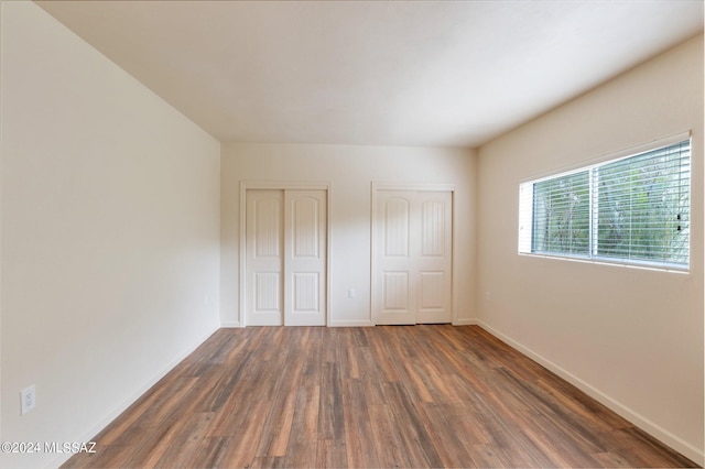 unfurnished bedroom with dark hardwood / wood-style flooring and two closets