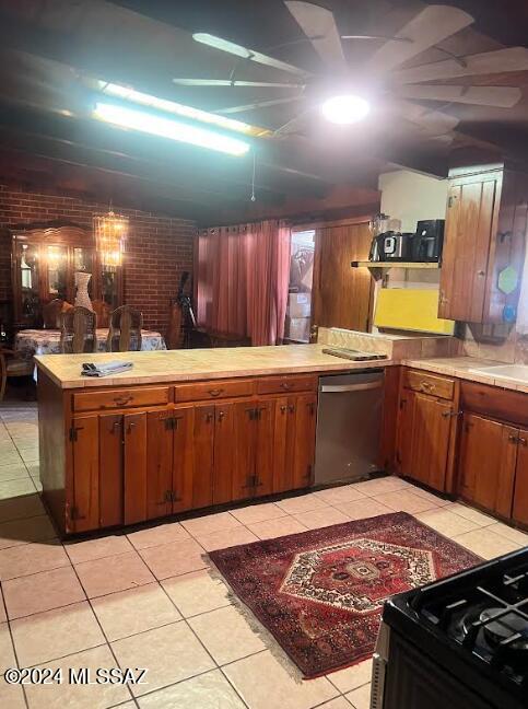 kitchen featuring light tile patterned flooring, stainless steel dishwasher, brick wall, and kitchen peninsula