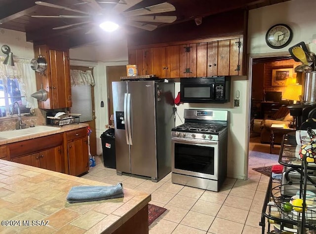 kitchen with light tile patterned floors, tile counters, appliances with stainless steel finishes, and sink